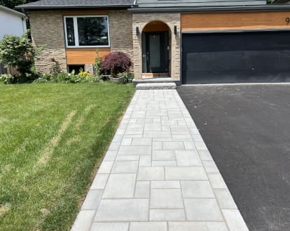 Long front walkway consisting of rectangular paver stones in varying sizes and colours beside a paved driveway, exemplifying Interlocking Driveway Extensions work on a large area