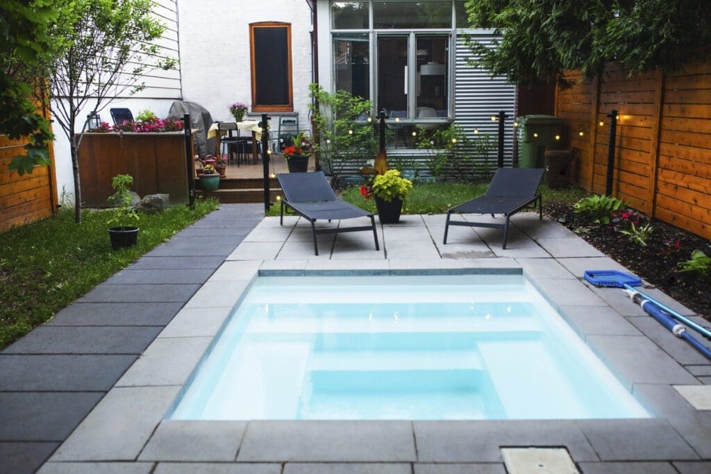 Modern backyard patio with interlocking stone, plunge pool, lounge chairs and string lights, ideal for summer entertaining and outdoor living.