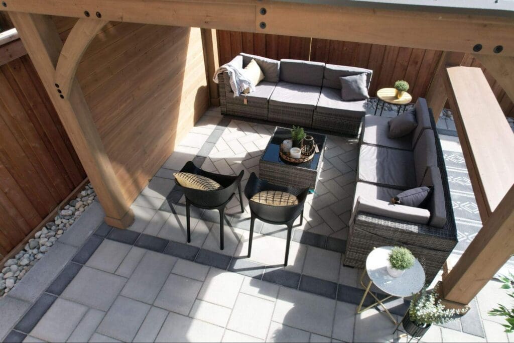 Covered backyard stone patio with herringbone interlocking pattern, lounge seating and cozy fall accessories.