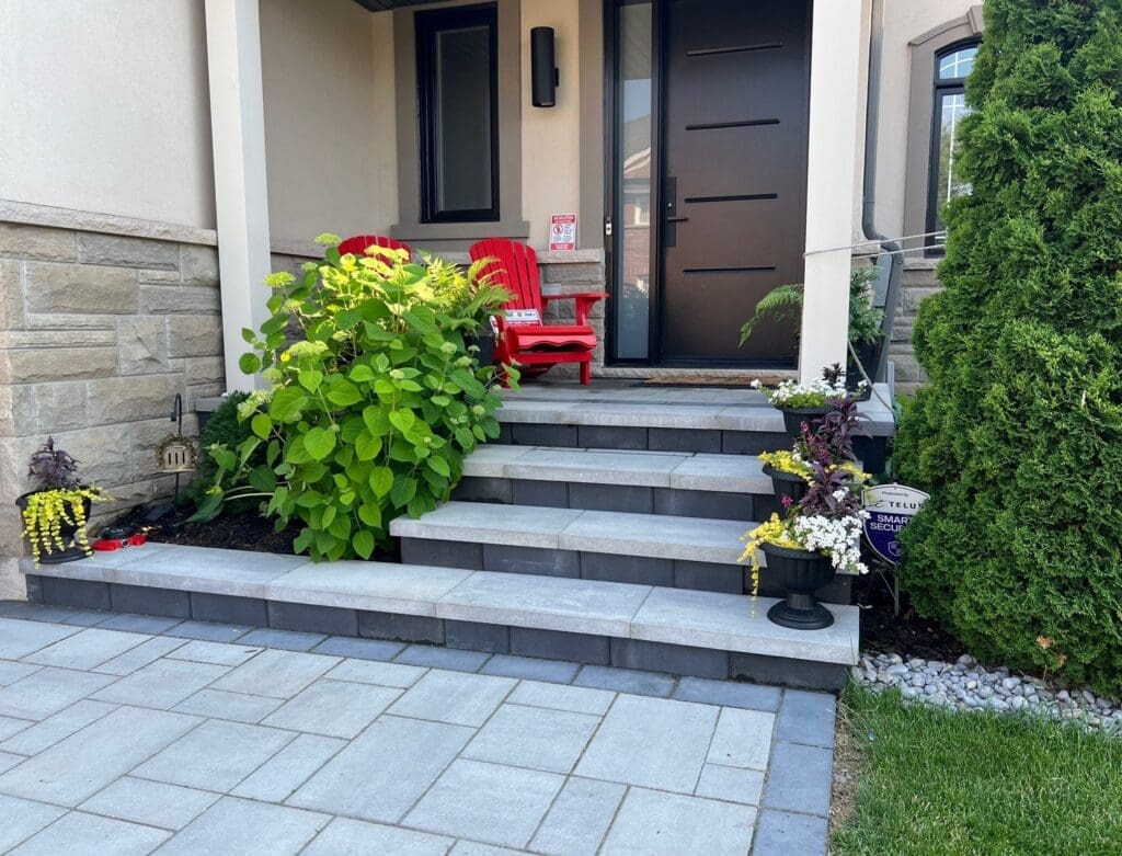 Front entrance of a home with interlocking stone steps, red patio chairs and potted plants along the walkway.