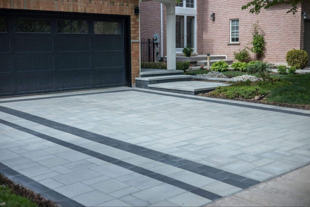 Modern interlocking driveway with light grey pavers and dark border accents in front of a suburban home