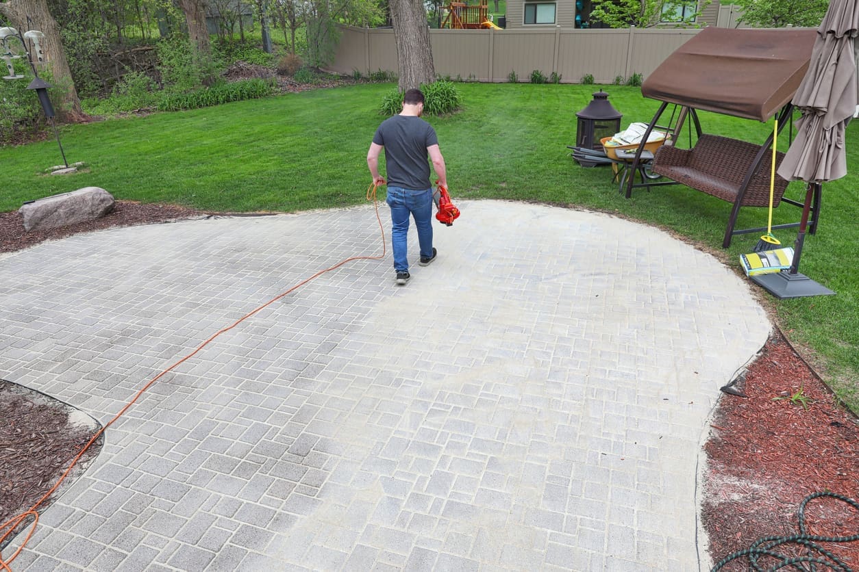 Interlocking patio maintenance showing joint sand application on paver surface.