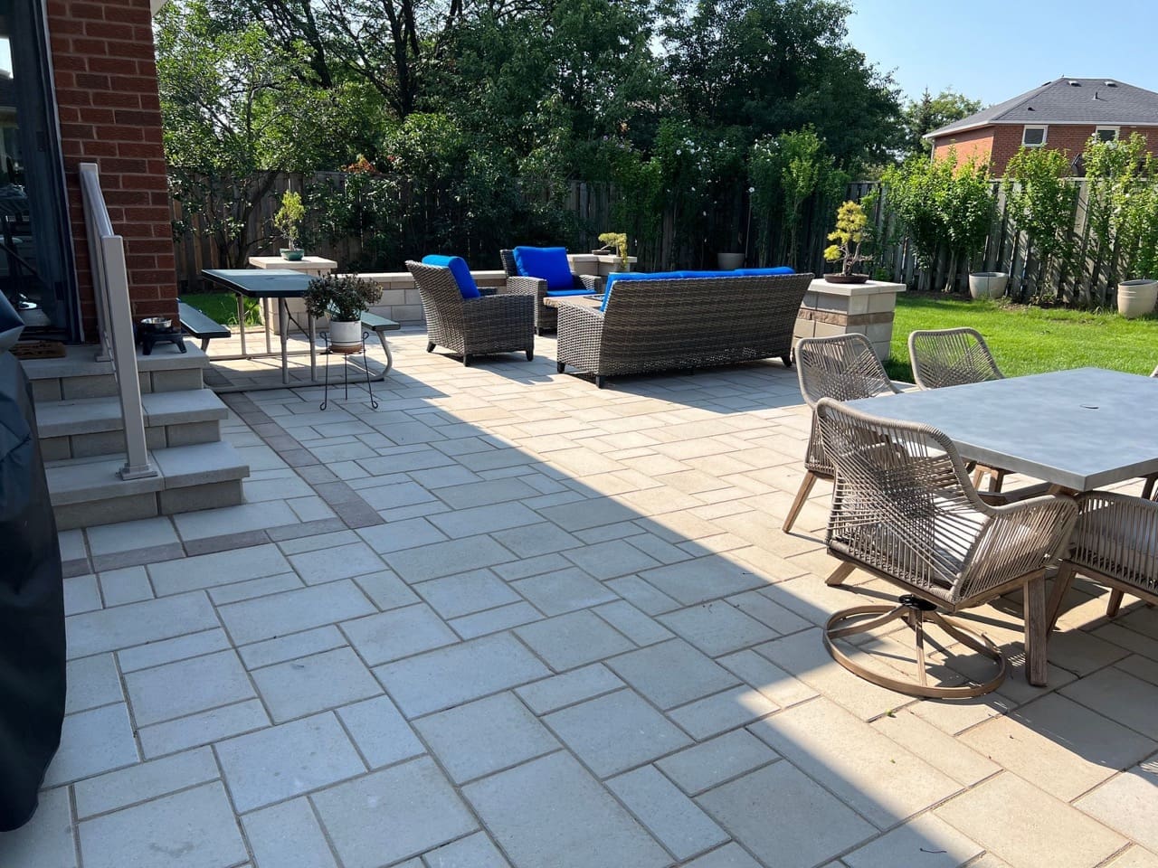 Backyard interlock design with large-format pavers, outdoor dining set, wicker lounge seating and lush landscaping.